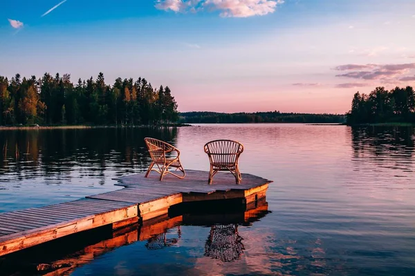 Due sedie in legno su un molo di legno che si affaccia su un lago al tramonto — Foto Stock