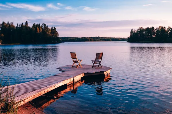 Två trästolar på en trä brygga med utsikt över en sjö vid solnedgången — Stockfoto