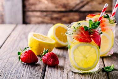 Ahşap arka plan üzerinde mason kavanozların içinde limon ve çilekli limonata.