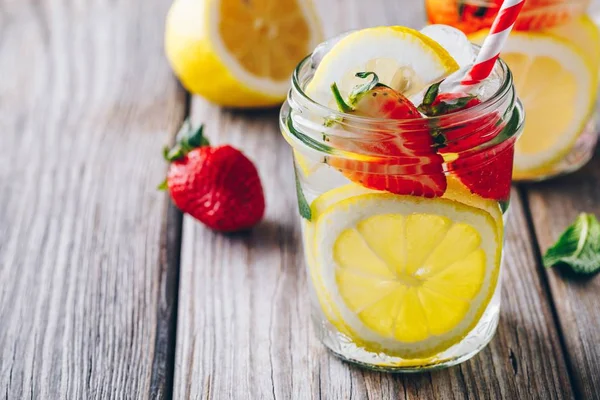 Lemon and strawberry lemonade in glass mason jars on a wooden background.