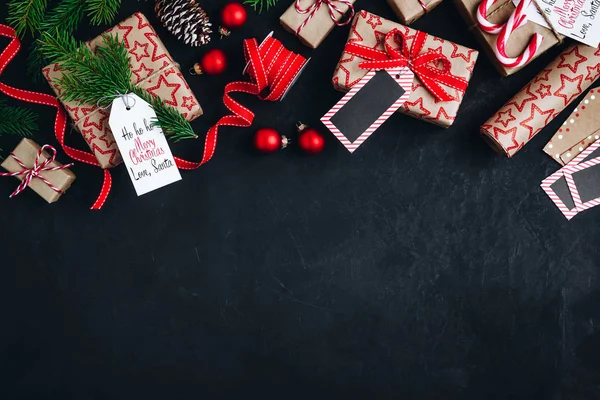 Noel arkaplanı köknar dalları ve koni hediye kutuları. Koyu beton arka planda kırmızı kurdele.. — Stok fotoğraf