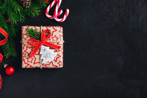 Sfondo natalizio con rami di abete e una scatola regalo con un fiocco rosso su uno sfondo di cemento scuro . — Foto Stock
