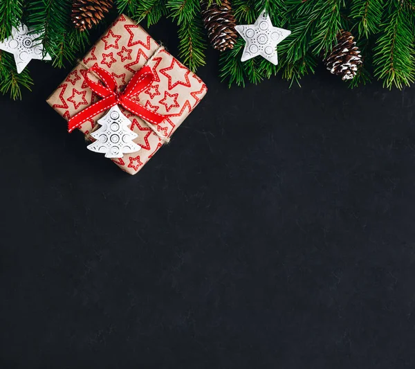 Sfondo natalizio con rami di abete e una scatola regalo con un fiocco rosso su uno sfondo di cemento scuro . — Foto Stock