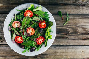 Taze yeşil salata yapraklarıyla roka, marul, ıspanak, pancar ve domateslerin ahşap arka planda karışımı..