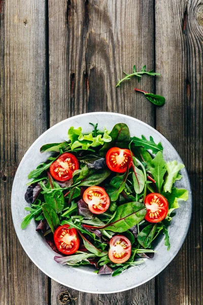 Mix of fresh green salad leaves with arugula, lettuce, spinach, beets and tomatoes on wooden rustic background. — Stock Photo, Image