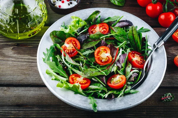 Mix of fresh green salad leaves with arugula, lettuce, spinach, beets and tomatoes on wooden rustic background. — Stock Photo, Image