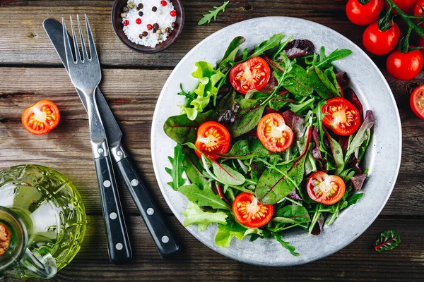 Mélange de feuilles de salade vertes fraîches avec roquette, laitue, épinards, betteraves et tomates sur fond rustique en bois . — Photo