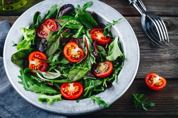 Miscela di foglie fresche di insalata verde con rucola, lattuga, spinaci, barbabietole e pomodori su fondo rustico in legno . — Foto Stock