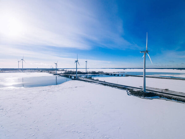 Aerial view of windmills with blue frozen river in snow winter Finland. Wind turbines for electric power 