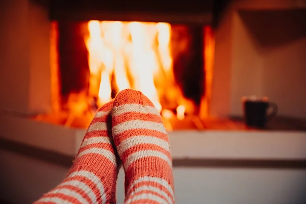 Feet in wool striped socks by the fireplace. Relaxing at Christmas fireplace on holiday evening. — Stock Photo, Image