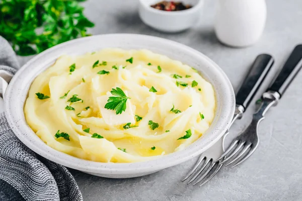 Mosade potatis med smör och färsk persilja i en vit skål på grå sten bakgrund. — Stockfoto