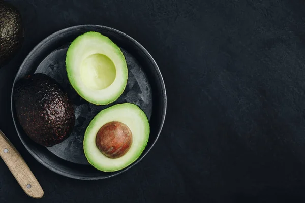 Avocado crudo su sfondo di pietra scura. Avocado fresco verde maturo per guacamole . — Foto Stock