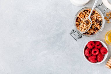 Sağlıklı kahvaltı gevreği, taze ahududu ve ballı gri taşlı arka plan.