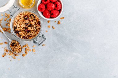 Sağlıklı kahvaltı gevreği, taze ahududu ve ballı gri taşlı arka plan.