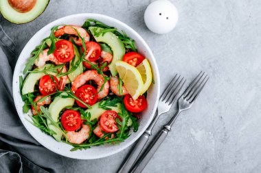 Sağlıklı roka salatası kasesi, karides, avokado, domates ve gri taş arka planda susam tohumu.. 