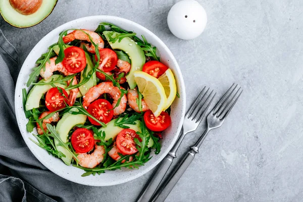 Healthy arugula salad bowl with shrimp, avocado, tomato, and sesame seeds on gray stone background. — 스톡 사진