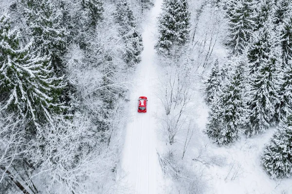 Vista superior aérea del bosque cubierto de nieve con carretera de invierno y coche rojo . —  Fotos de Stock