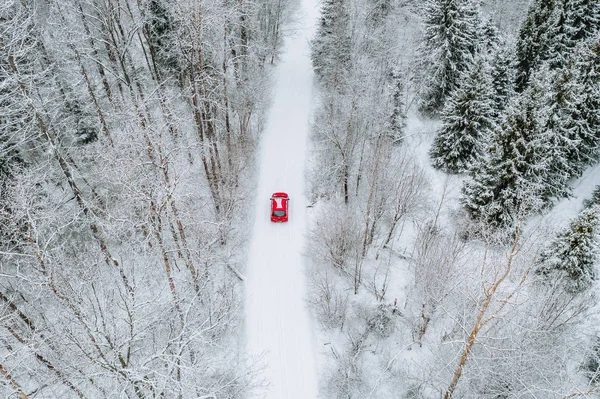 Widok z lotu ptaka pokryty śniegiem las z drogi zimowej i czerwony samochód. — Zdjęcie stockowe