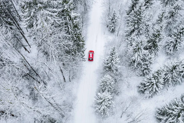 Vista superior aérea del bosque cubierto de nieve con carretera de invierno y coche rojo . —  Fotos de Stock