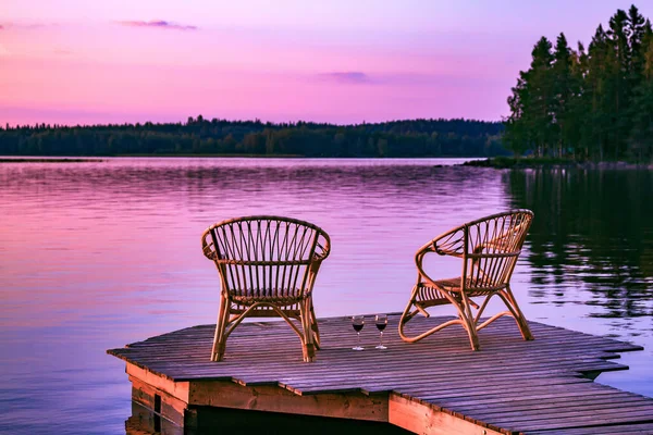 芬兰落日时分 码头上俯瞰湖面的两张藤椅和几杯红酒 — 图库照片