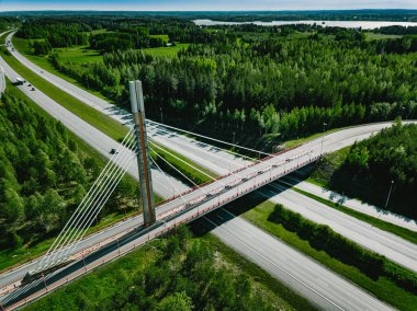 Finlandiya 'da yaz günü yeşil ormanlı otoban ve asma köprü manzarası.