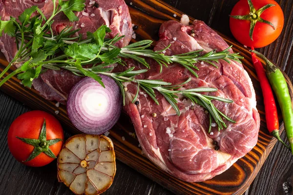 Siyah taştan bir tabakta taze kuzu boynu, baharatlar ve taze sebzelerle.