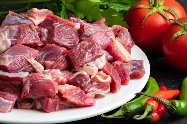 Beyaz bir tabakta taze sebzelerle birlikte çiğ et parçaları.