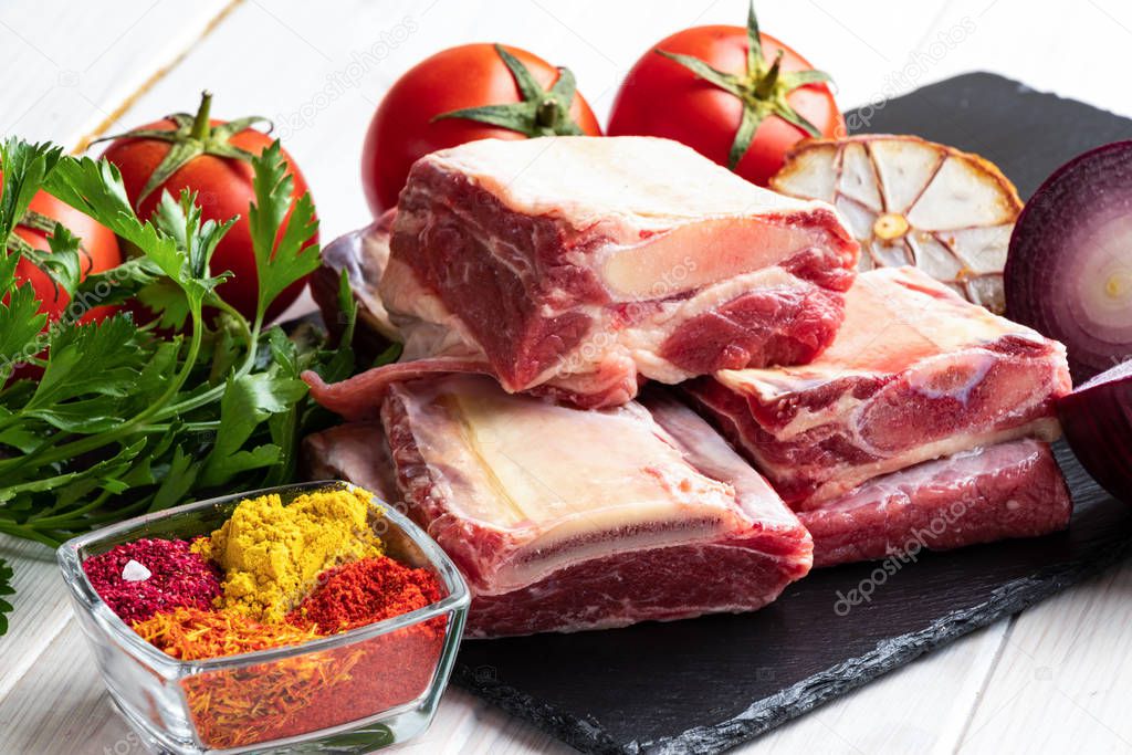 Raw meat. Beef ribs on a wooden cutting board with spices and fresh vegetables.