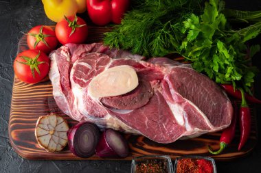 Koyu arkaplanda taze sebzeler ve baharatlarla büyük bir parça çiğ et.