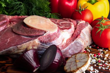 Koyu arkaplanda taze sebzeler ve baharatlarla büyük bir parça çiğ et.