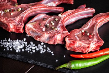 Çiğ et, kuzu kaburgası, siyah taş arka planda otlar, baharatlar ve taze sebzeler.