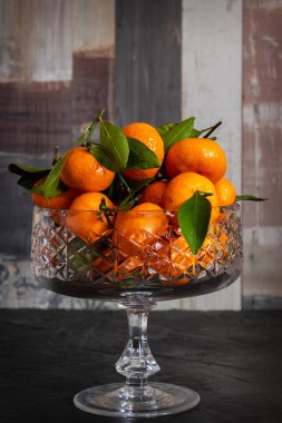 Mandalina mandalinası. Ahşap bir arka planda kristal bir vazoda yaprakları var..