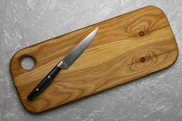 Knife on a wooden cutting board on a light gray stone table