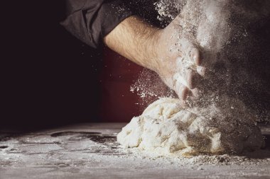 Adam el çırpıyor ve masaya taze hamur serpiyor. Yemek konsepti. Uzayı kopyala Tonu ayarlanmış resim