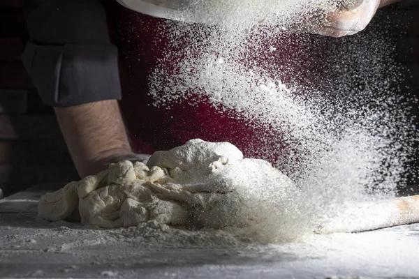 A man, a chef sprinkles flour on a dough through a sieve. Close-up. Dark background