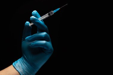 Mavi eldivenli doktorun elinde siyah arka planda bir şırınga var. Yakın plan. Metin için yer