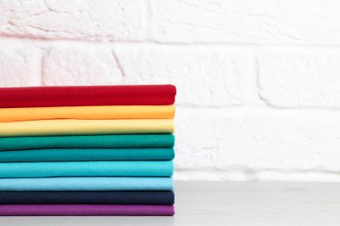 Temiz, düzgün katlanmış renkli giysiler, açık ahşap bir masanın üzerinde. Gökkuşağının renkleri. Metin için yer