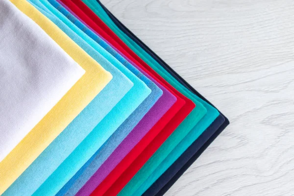 Temiz, düzgün katlanmış renkli giysiler, açık ahşap bir masanın üzerinde. Gökkuşağının renkleri. 