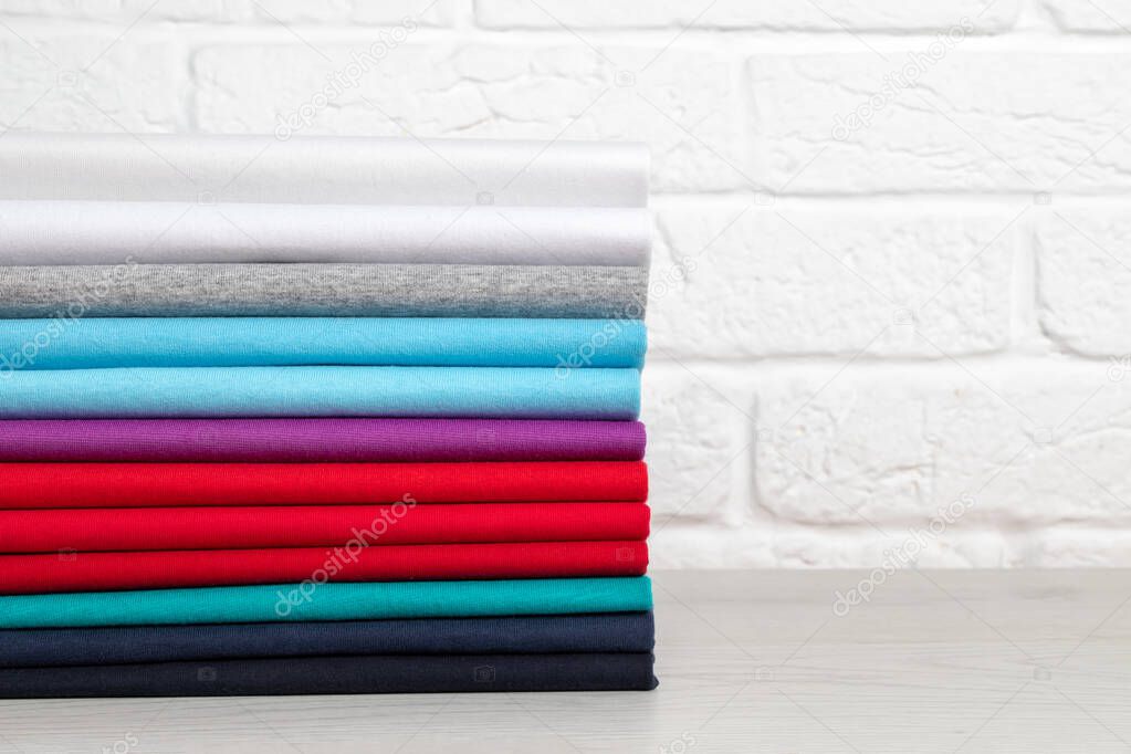 A stack of clean, neatly folded colored clothes on a light wooden table. Colors of rainbow. Place for text