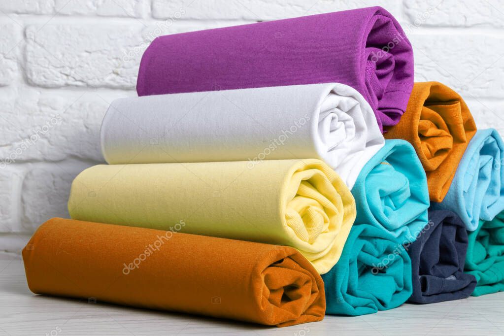 Stack of colored rolled clothes on a light wooden table. Close-up