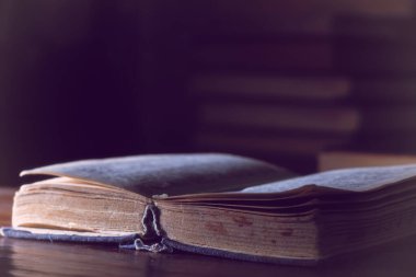 Çok eski bir kitabı ahşap bir masanın üzerinde bir yığın kitabın arka planına karşı aç