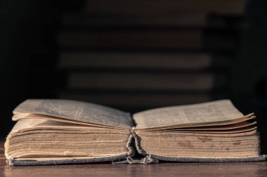 Çok eski bir kitabı ahşap bir masanın üzerinde bir yığın kitabın arka planına karşı aç