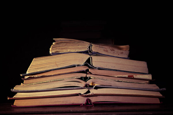 A stack of very old open books close-up on a dark background. Vintage effect