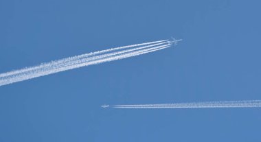 İki uçak mavi gökyüzünde uçuyor, arkasında motorların beyaz çizgilerini bırakarak. Ters dönüş, atmosferdeki jet pisti..
