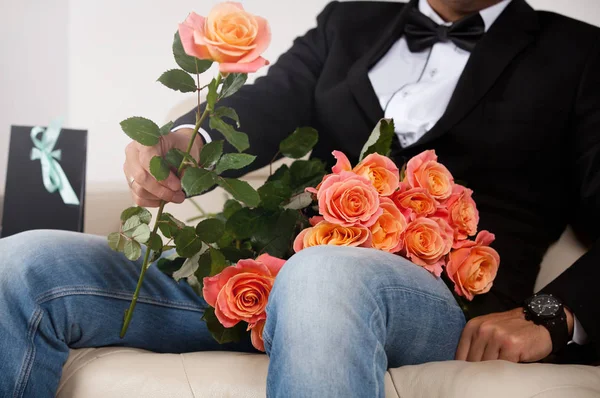 Eleganter junger schöner Mann im schwarzen Anzug mit Rosenstrauß. Stockbild