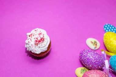 Renkli Paskalya yumurtaları ve çöreklerden oluşan pembe bir arka planda.