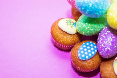 Renkli Paskalya yumurtaları ve çöreklerden oluşan pembe bir arka planda.