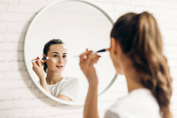 Woman applying makeup in bathroom.