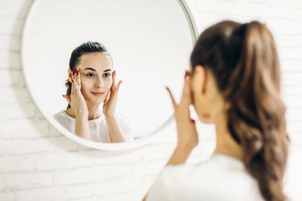 The woman is making up in the bathroom. Woman in bathroom applying cream on face.