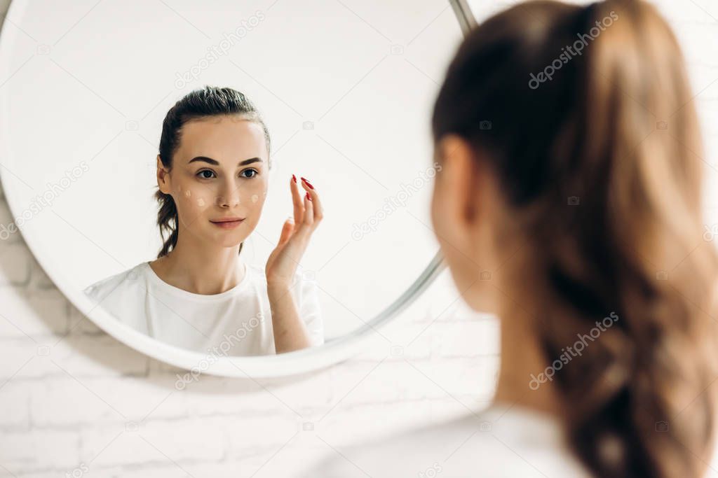 The woman is making up in the bathroom. Woman in bathroom applying cream on face.